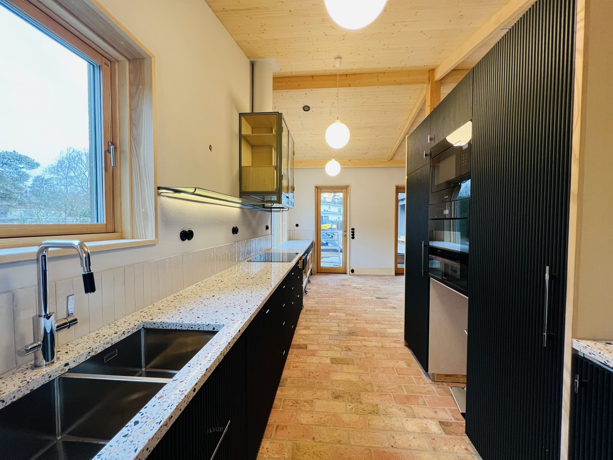 Platsbyggt svart kök med lång härlig bänkskiva utan överskåp