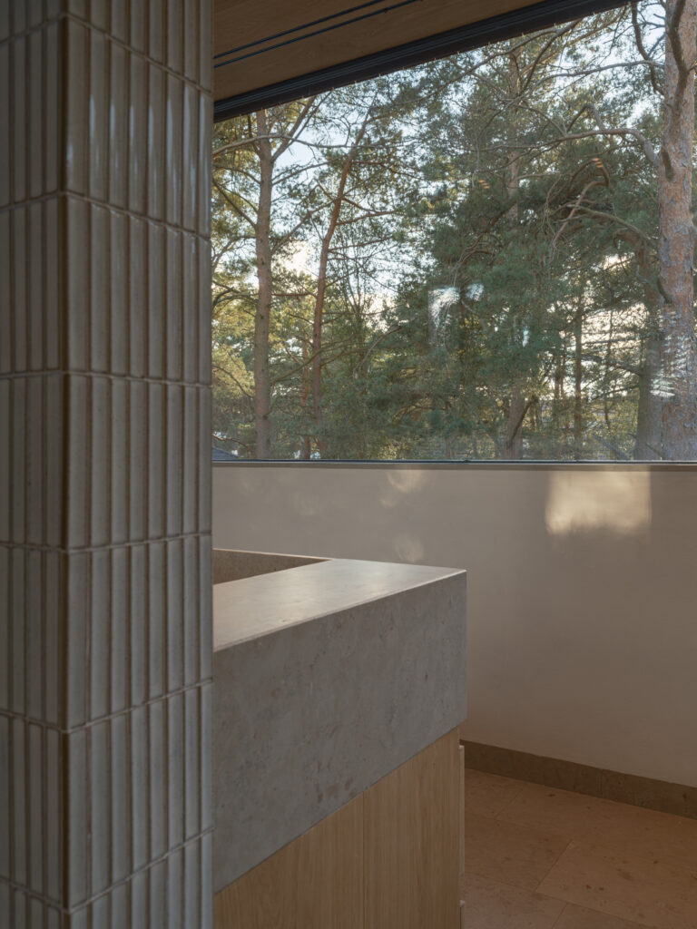 Exklusivt badrum i Villa P2 med väggar och inredning i trä och sten, stort fönster och takfönster i duschen som släpper in naturligt ljus. Harmonisk design med noggrant utvalda material och tidlös elegans.